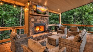 Una terraza exterior con una chimenea de piedra, mobiliario de mimbre y un televisor montado sobre la chimenea.