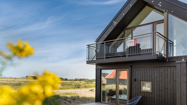 A modern two-story house with a balcony, large windows, and a wooden deck. - Ocean front home in Skagen with WiFi (Skagen)