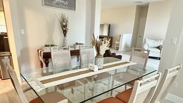 A dining area with a glass-top table, white chairs, and a chandelier.