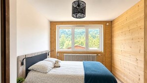 Et soveværelse med en seng, et vindue med udsigt til træer, en radiator og en hængende lampe.
