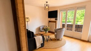 En rummelig stue med træloft, en sofa, en lænestol, et lille bord og et fjernsyn.