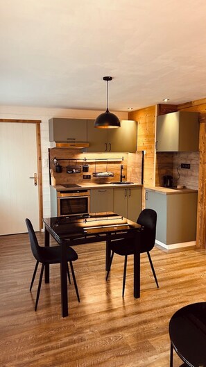 Una cocina moderna con armarios de madera, una isla central y una zona de comedor con mesa de cristal y sillas negras.
