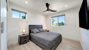 A modern bedroom with a bed, nightstands, a ceiling fan, and windows with a view.