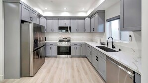 A modern kitchen with grey cabinets, stainless steel appliances, and a marble countertop.