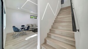 A modern interior with a staircase, a dining area with a table and chairs, and a sofa.