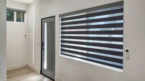 A hallway with a sliding glass door, a large window with horizontal blinds, and a light switch on the wall.