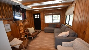 Een gezellig interieur van een chalet met houten details, een bank, een stoel, een televisie en een raam met jaloezieën.