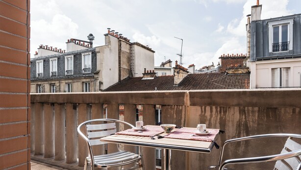 Un balcón con dos sillas de metal y una mesa, con vistas a una hilera de edificios de estilos arquitectónicos variados.