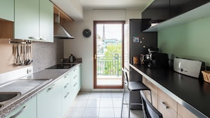 Una cocina moderna con armarios verde claro, encimera negra y vistas a la Torre Eiffel a través de una puerta.