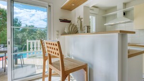 Une cuisine moderne avec une grande fenêtre, une table à manger en bois et une vue sur une piscine et des arbres.