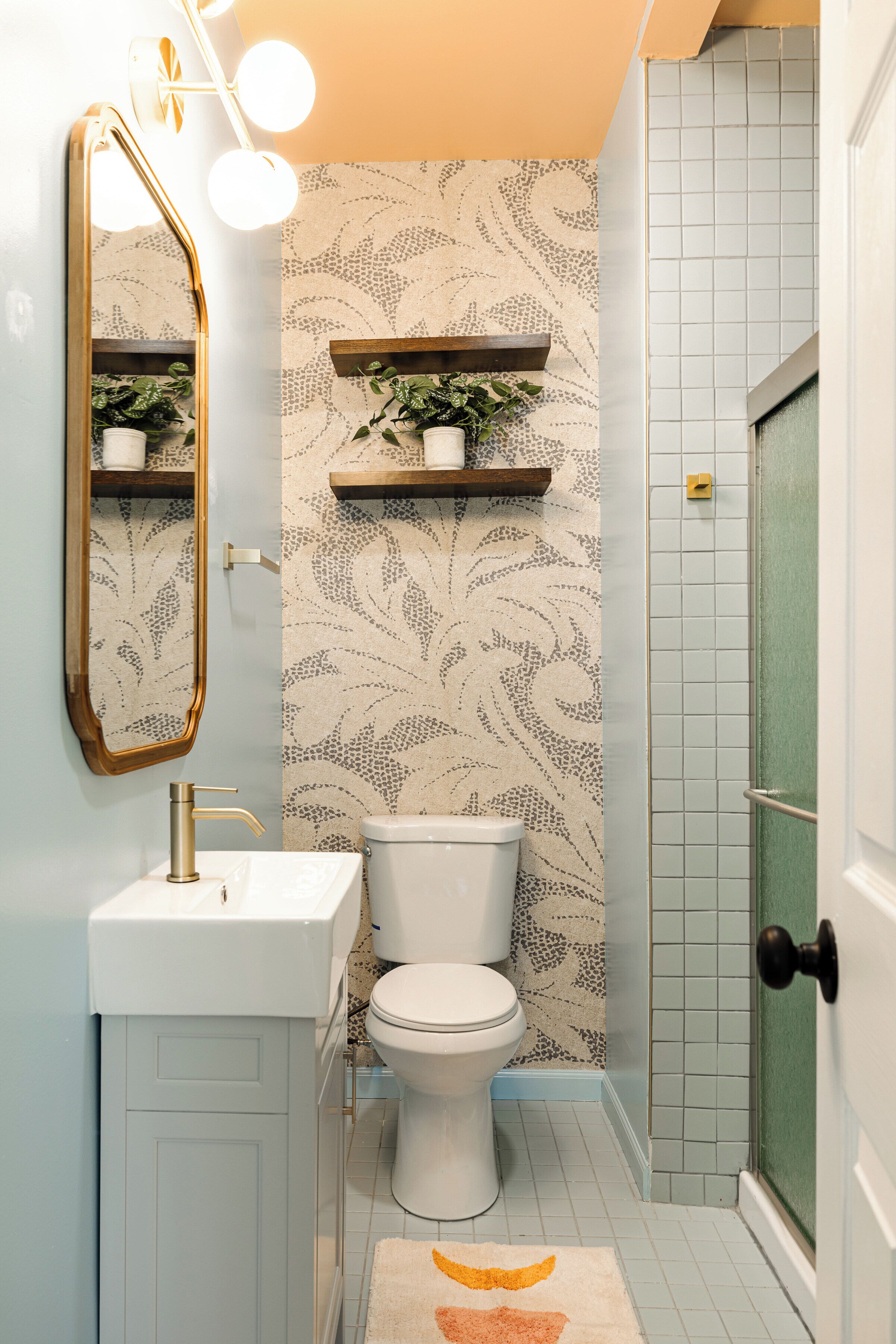 Une salle de bain avec un lavabo blanc, des toilettes, un miroir avec éclairage intégré et un papier peint à motifs.