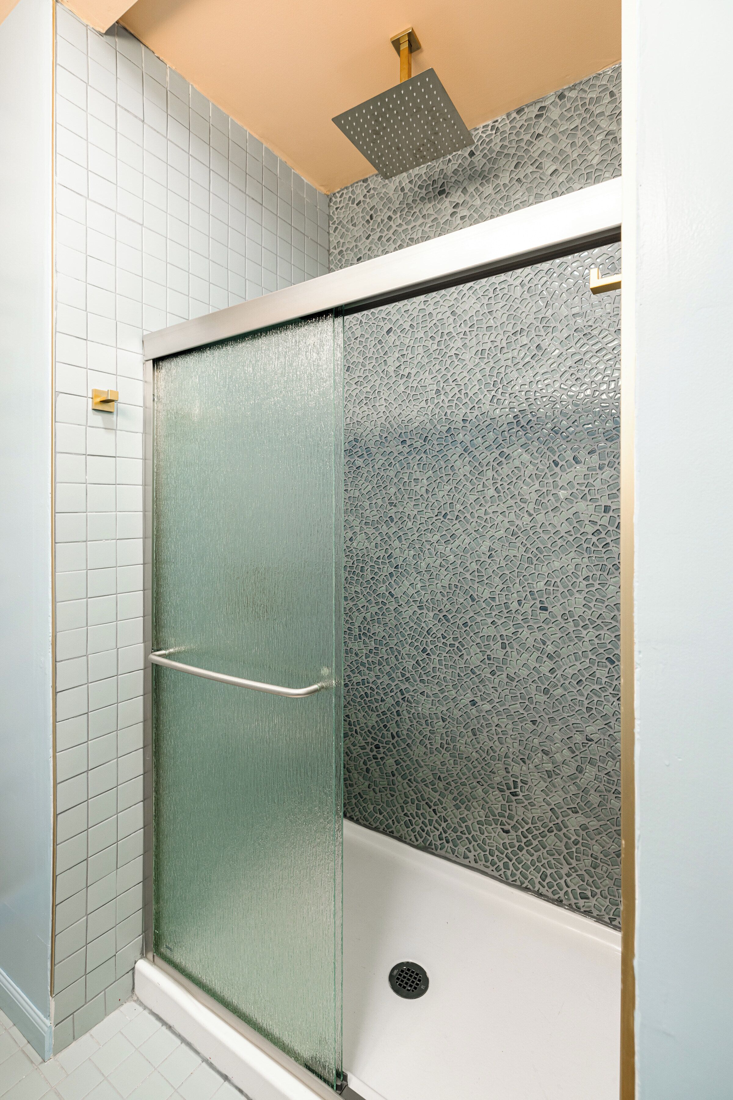 Un box de ducha con puerta de vidrio esmerilado, un pomo de metal y una pared con relieve.
