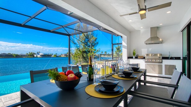 Una cocina moderna con vista al mar, una mesa de comedor con frutas y bebidas, y un ventilador de techo.