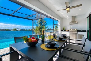 A modern kitchen with a view of the sea, a dining table with fruit and drinks, and a ceiling fan. - VILLA STINGRAY – HEATED POOL & SPA | LAKE VIEW | BOAT RENTAL + TOURS VOUCHER INCL. (Cape Coral)