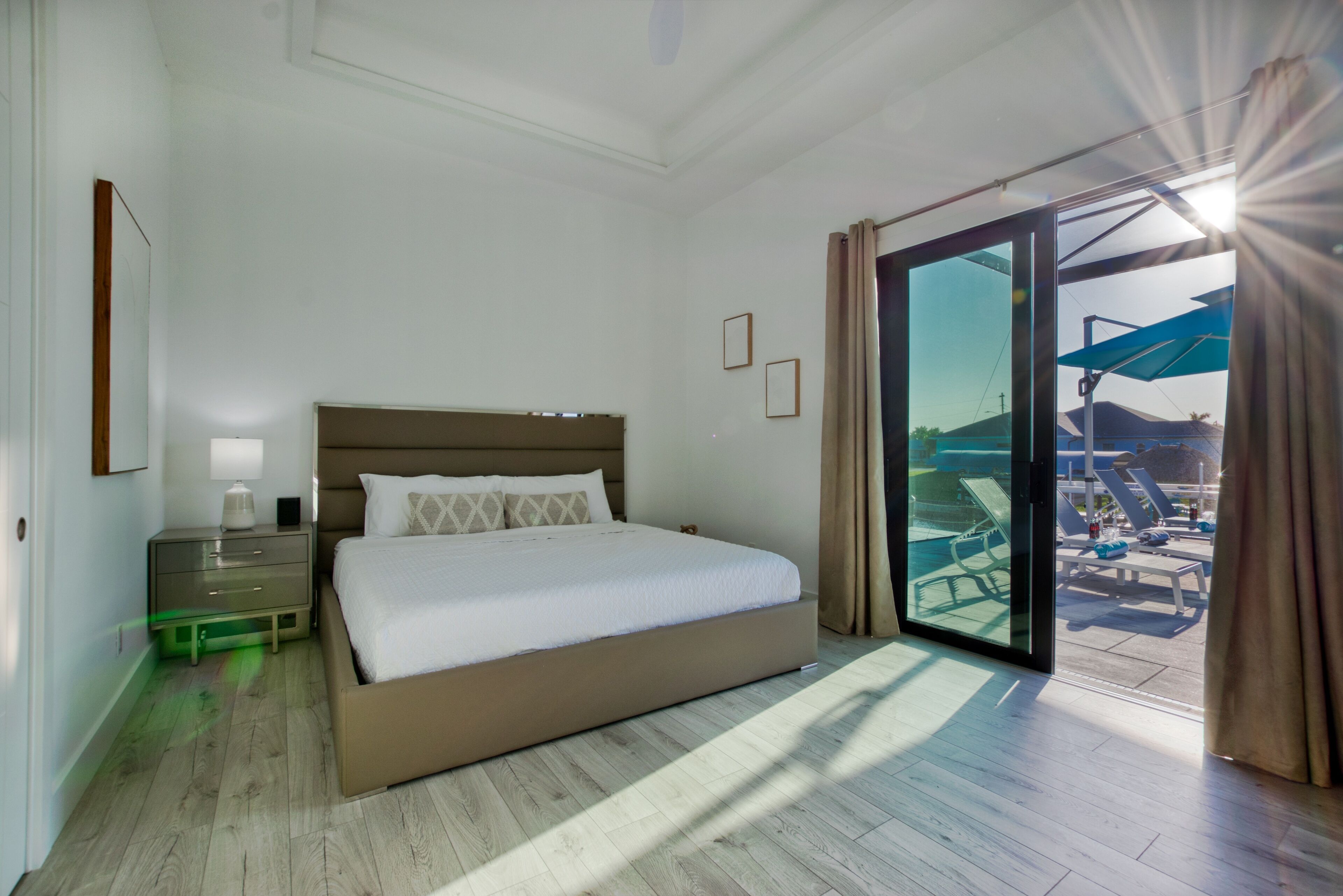 Une chambre d’hôtel avec un grand lit, une table de chevet, une lampe et une vue sur l’espace piscine, accessible par une porte-fenêtre coulissante.