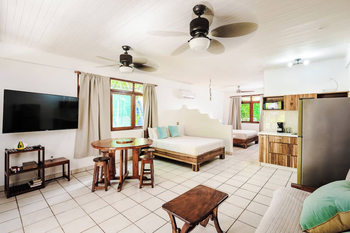 A spacious living area with a sofa, a dining table with stools, a TV, and ceiling fans.
