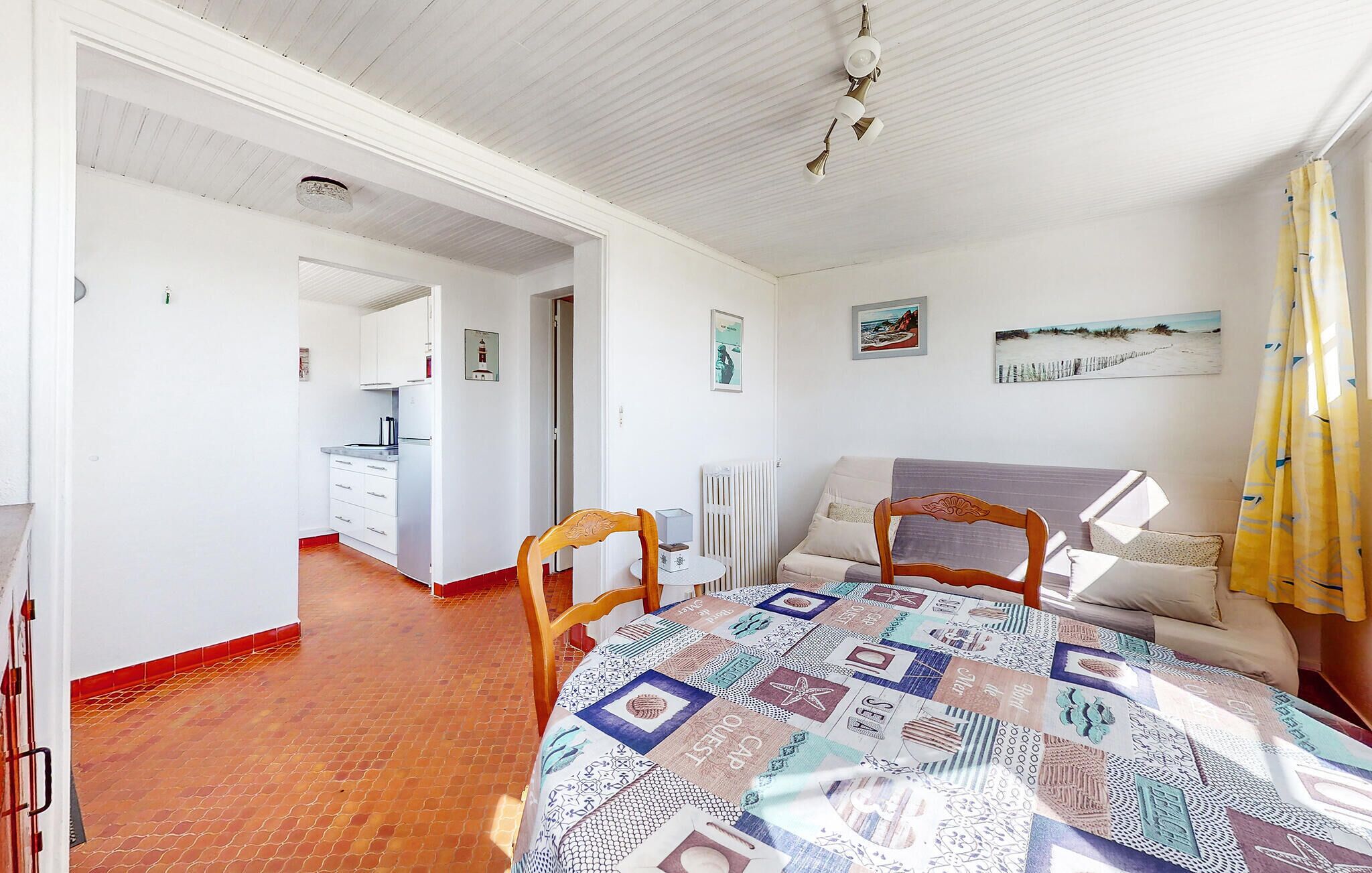A room with a dining table, two chairs, a sofa, a radiator, and a kitchen in the background.