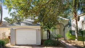 A residential house with a garage, a paved driveway, and a large tree in front. - Lake View Pool Home With Game Room (Haines City)
