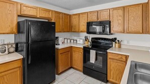 A kitchen with wooden cabinets, a black refrigerator, a microwave, a stove, and a sink. - Lake View Pool Home With Game Room (Haines City)