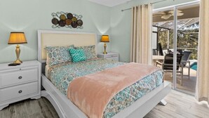 A bedroom with a bed, two bedside tables, a wall decoration, and a view of an outdoor area with a pool and chairs. - Lake View Pool Home With Game Room (Haines City)