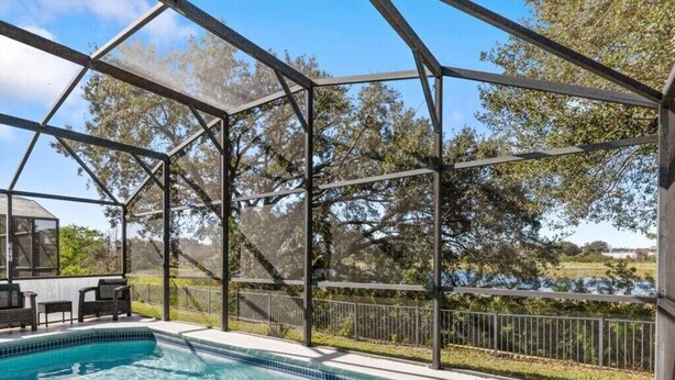 A covered outdoor swimming pool with a clear view of the surrounding landscape and trees. - Lake View Pool Home With Game Room (Haines City)
