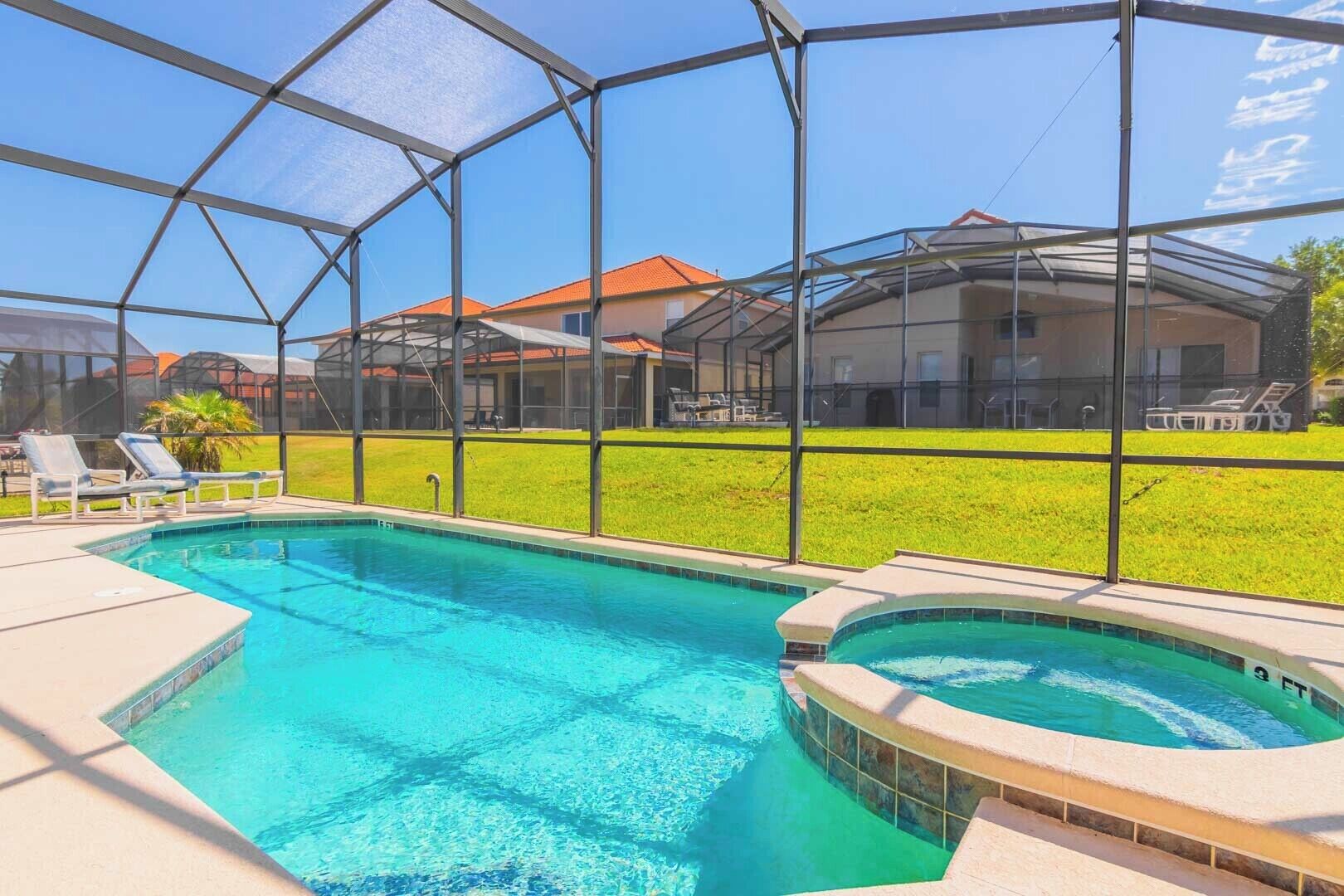 Ein Schwimmbad mit Glasumrandung, umgeben von einer Rasenfläche und einem Haus im Hintergrund.