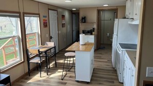 A compact kitchen with a dining area, wooden flooring, and large windows. - Prairie Tiny Home near TRNP (Belfield)