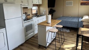 A compact kitchen with a refrigerator, stove, and bar stools. - Prairie Tiny Home near TRNP (Belfield)