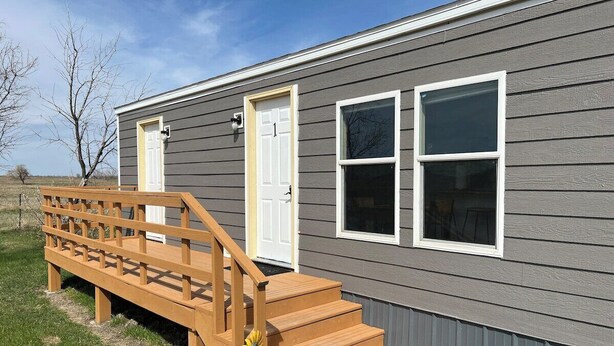A single-story house with a wooden deck and a front door. - Prairie Tiny Home near TRNP (Belfield)