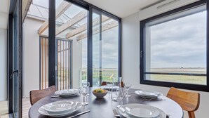 Une table à manger dressée pour quatre personnes, avec vue sur la campagne grâce à de grandes fenêtres.