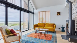 Un salon spacieux avec de grandes fenêtres, un canapé jaune, un tapis à motifs et une cheminée moderne.