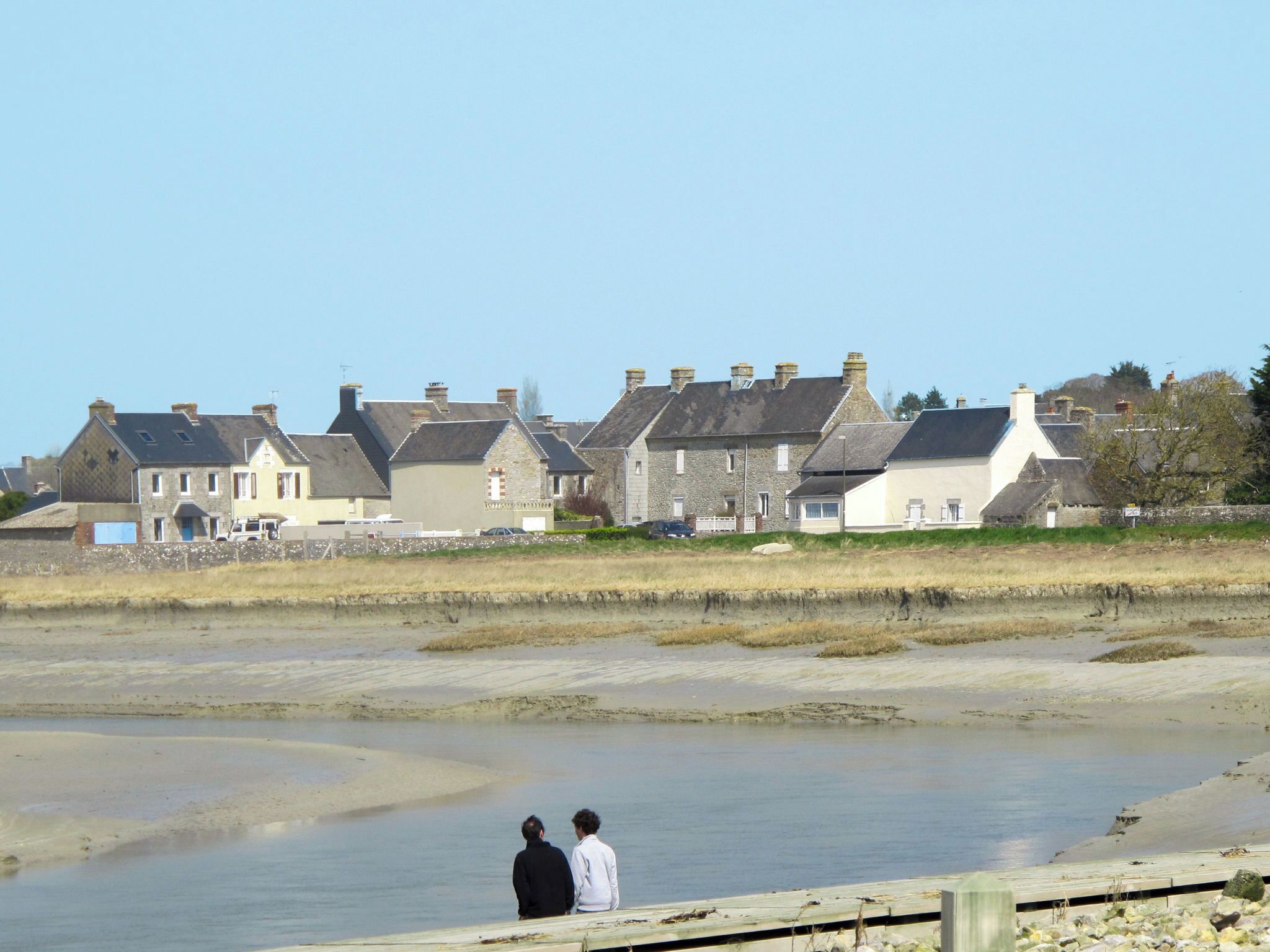 A coastal town with stone houses, a sandy beach, and two people standing by the water.