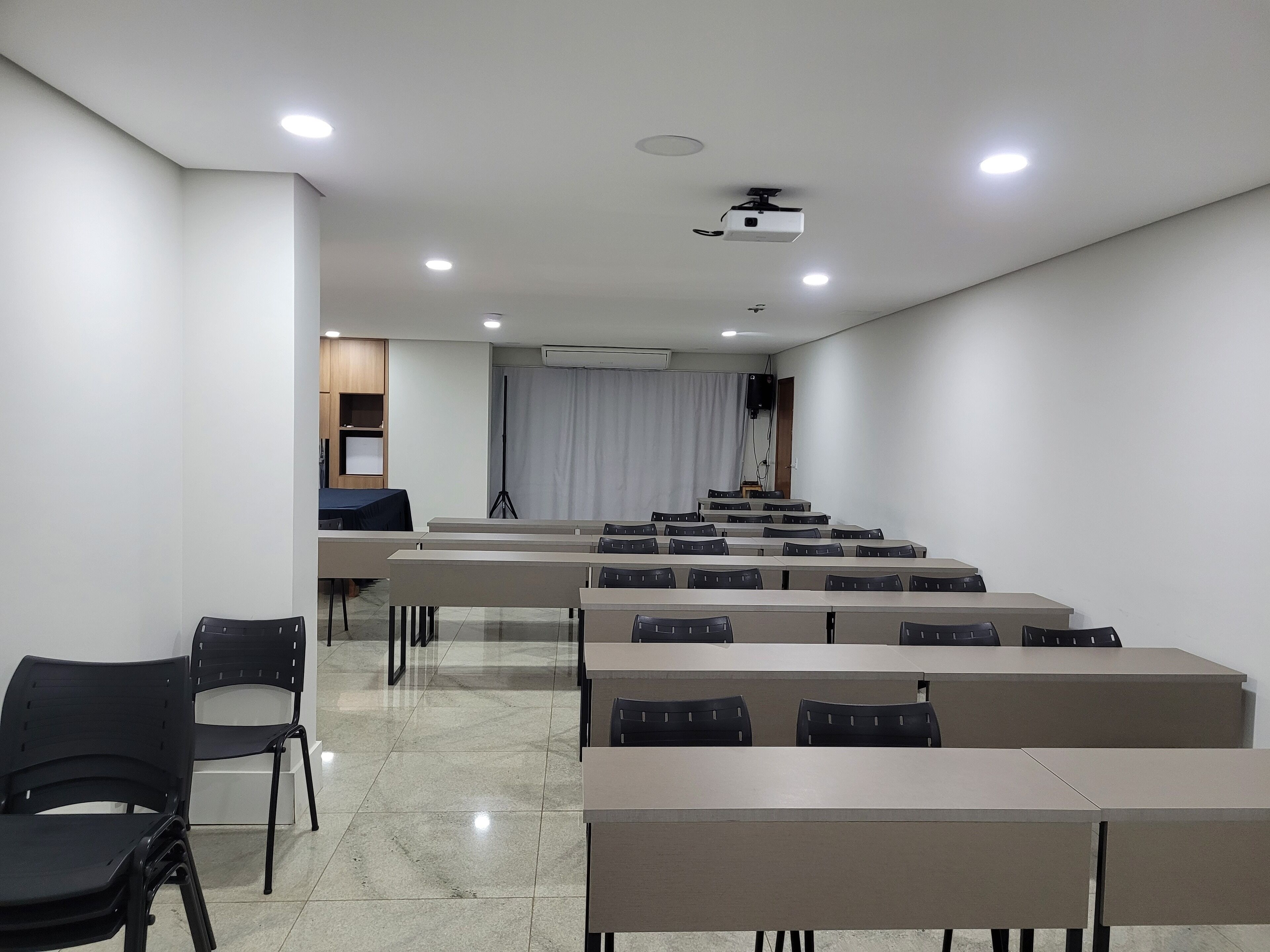 A conference room with rows of tables and chairs, a projector, and a curtain backdrop.