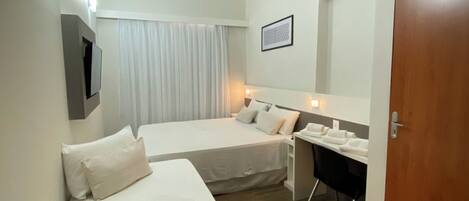 Ein Hotelzimmer mit zwei Betten, einem Schreibtisch, einem Stuhl, einem kleinen Tisch, einem Spiegel, einem Bild an der Wand und einer Tür.