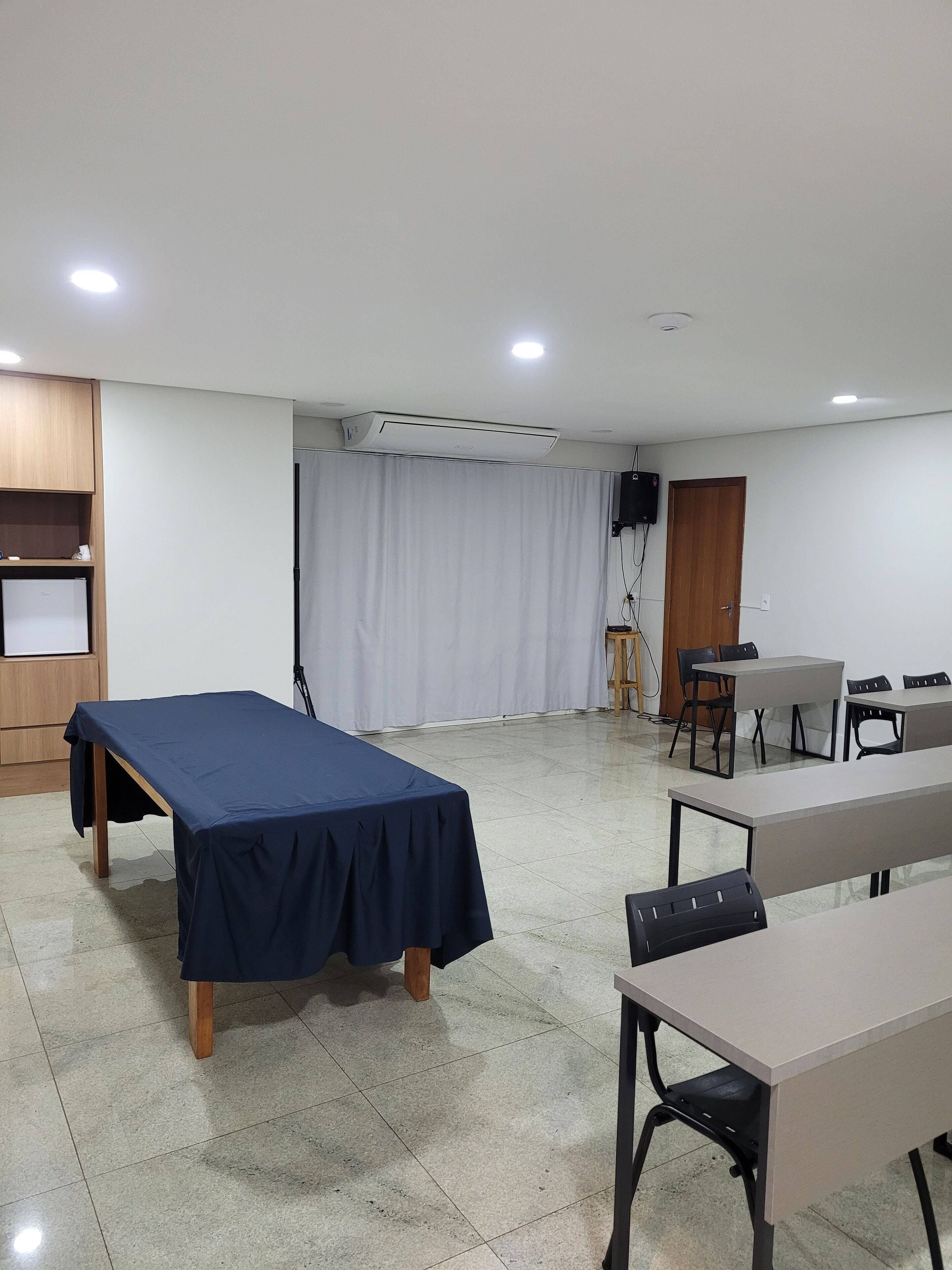 Une salle de conférence avec une longue table recouverte d’une nappe sombre, un écran de projection et un rideau blanc.