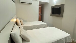 Une chambre avec deux lits, un appareil de climatisation, un téléviseur fixé au mur et un tableau encadré accroché au mur.
