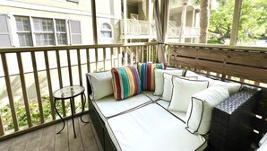 Ein Balkon mit gepolsterten Sitzgelegenheiten, einem kleinen Tisch und Blick auf ein Gebäude mit zahlreichen Fenstern und Balkonen.