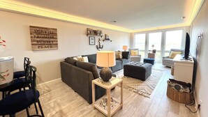 Ein modernes Wohnzimmer mit einem grauen Sofa, einem Holztisch und einem Essbereich mit Tisch und Stühlen.