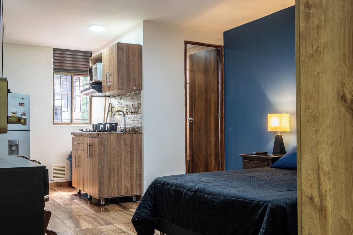 Una habitación pequeña con cama, una kitchenette y una puerta que da a otra habitación.