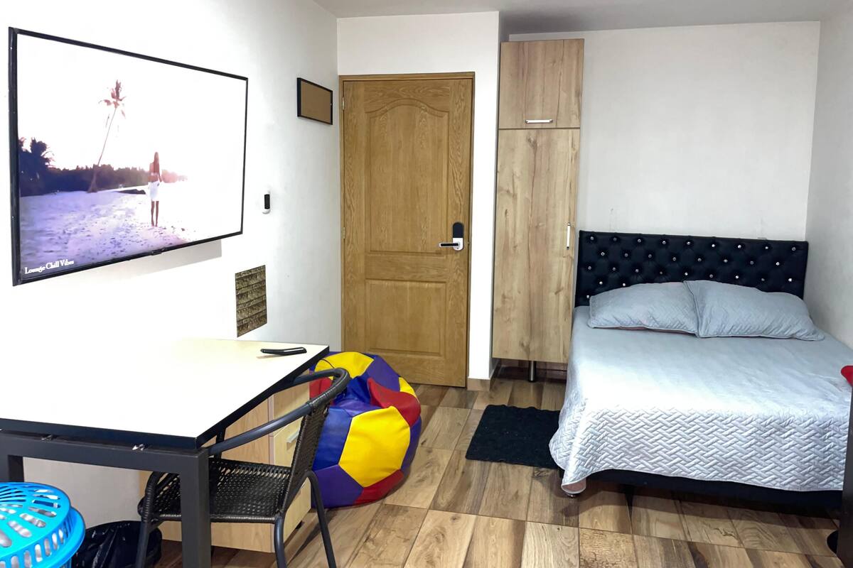 Un dormitorio con cama, escritorio, silla, armario y televisor.