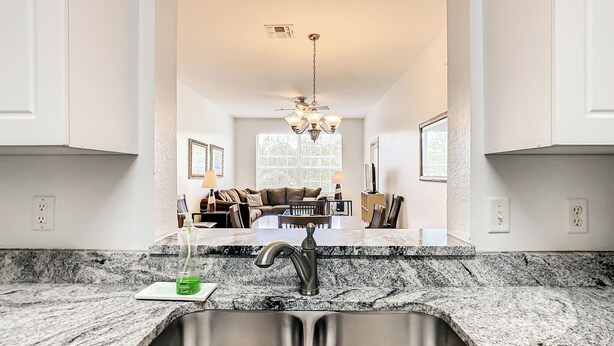 A kitchen with a double sink, granite countertops, a dining area with a sofa and chairs, and a chandelier. - 3 Bed Windsor Palms Condo - Conservation Views (Kissimmee)