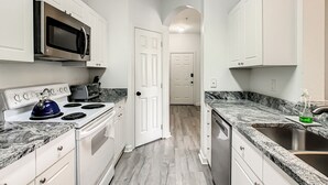 A modern kitchen with white cabinets, a stainless steel microwave, a stove, and a granite countertop. - 3 Bed Windsor Palms Condo - Conservation Views (Kissimmee)
