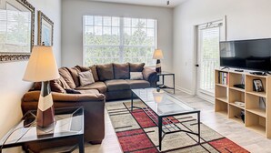 A modern living room with a sectional sofa, glass coffee table, and a TV on a wooden stand. - 3 Bed Windsor Palms Condo - Conservation Views (Kissimmee)