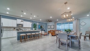 Une cuisine moderne avec des meubles blancs, un îlot central doté de tabourets et un coin repas avec une grande table et des chaises.