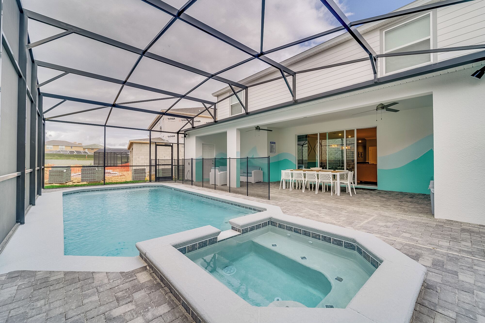 Ein Innenpoolbereich mit Whirlpool, einer überdachten Terrasse mit Sitzgelegenheiten und Blick auf die umliegenden Gebäude.