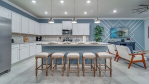 Une cuisine moderne avec des meubles blancs, un îlot central doté de tabourets et un éclairage suspendu.
