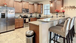 A modern kitchen with wooden cabinets, stainless steel appliances, a granite countertop, and a bar area with stools.