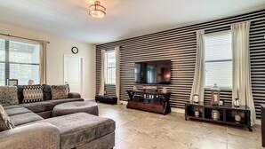 A living room with a sectional sofa, a flat-screen TV, and a striped wall.