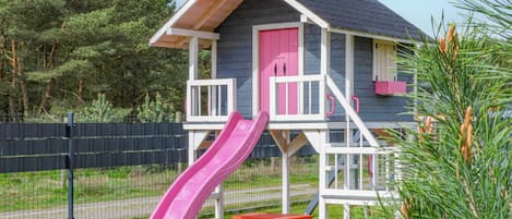 A children's playhouse with a pink slide, a red table, and a pink door.