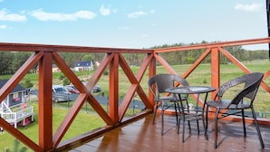 Eine Holzterrasse mit Metallgeländer, zwei Korbstühle und einem kleinen runden Tisch.